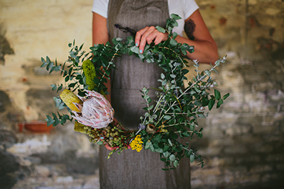 A guy in a grey apron holding a flower wreath